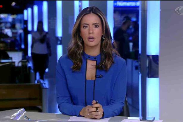 Paloma Tocci veste uma blusa azul sentada na bancada do Jornal da Band