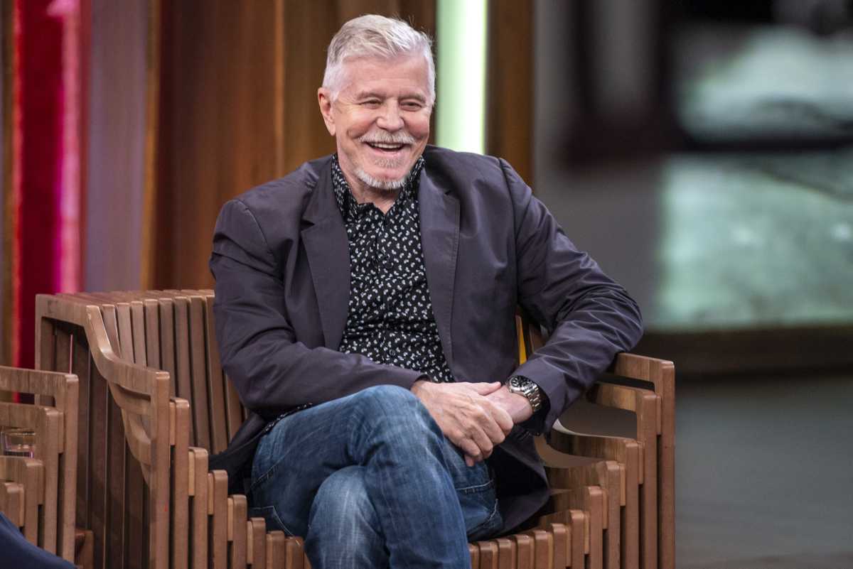 Miguel Falabella de calça jeans e blazer preto sentado em uma cadeira