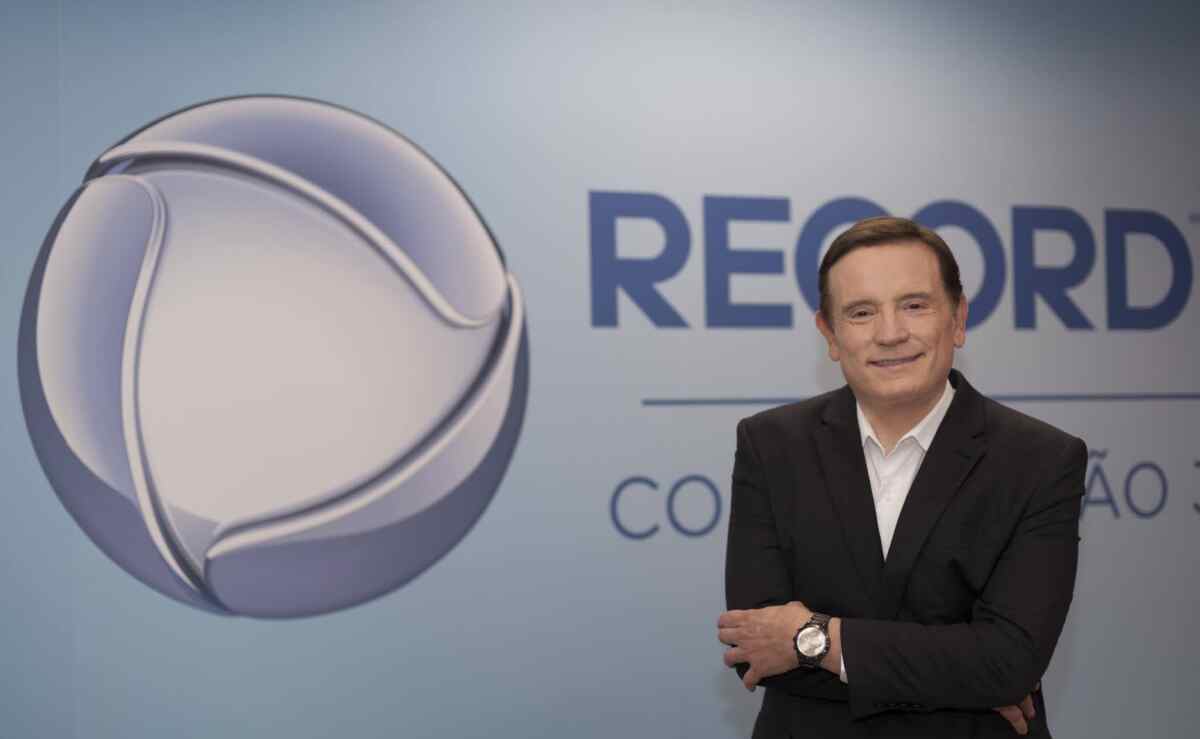 Roberto Cabrini em frente a um banner com o logo da Record TV