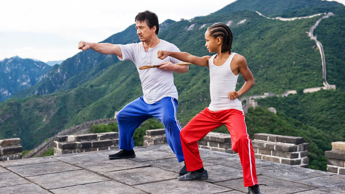 Atores Jaden Smith e Jackie Chan em cena do filme Karated Kid, com as pernas abertas em posição de luta. Os dois usam calças