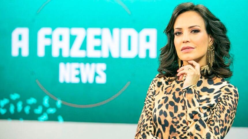 Fabiana Oliveira com a mão no queixo, posando para foto no cenário do programa A Fazenda News