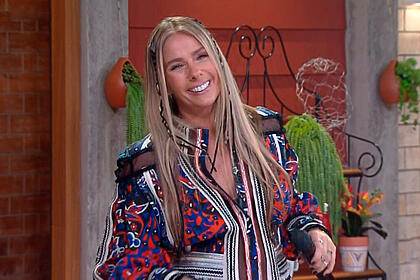 Adriane Galisteu sorrir segurando o microfone enquanto apresenta A Fazenda 13, ao vivo