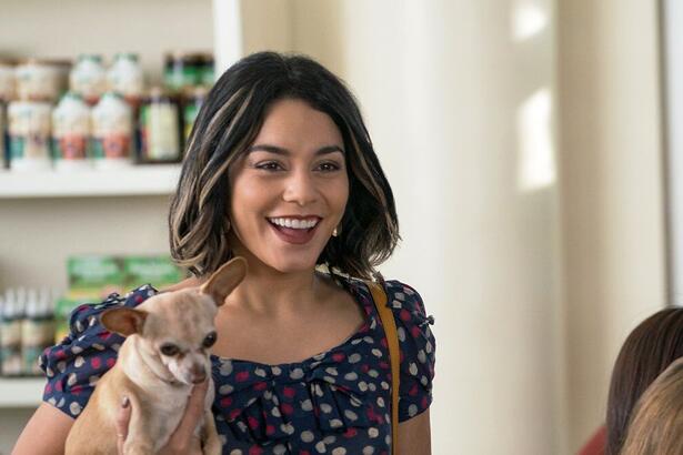 Mulher segura um pequeno cachorro com a mão e sorrir em cena do filme Nossa Vida com Cães