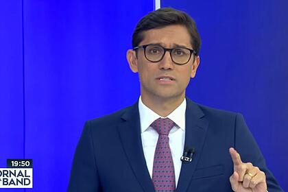 Rodolfo schneider nos estúdios do jornal da band, em frente ao telão, com dedo indicativo apontando para a tela
