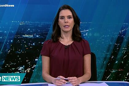 Camila Busnello sentada na bancada nos estúdios do Jornal da Record News
