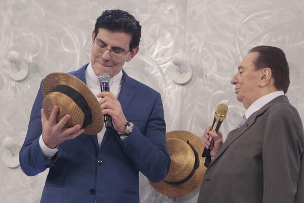 Padre Reginaldo Manzotti segurando um chapéu ao lado de Raul Gil, nos estúdios do programa