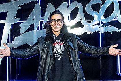 André Gonçalves de braços abertos em frente ao logo do Dança dos Famosos
