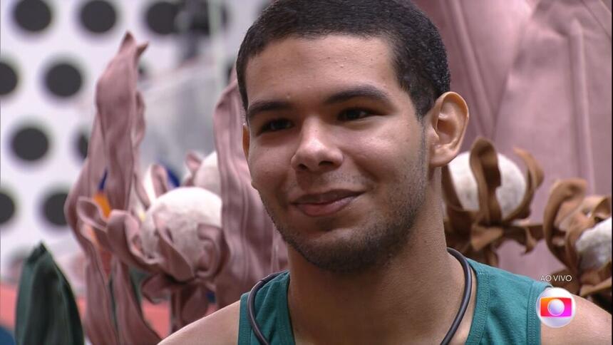 Vinicius sentado na sala do BBB 22 demonstra felicidade ao saber do resultado do primeiro jogo da discórdia do BBB 22