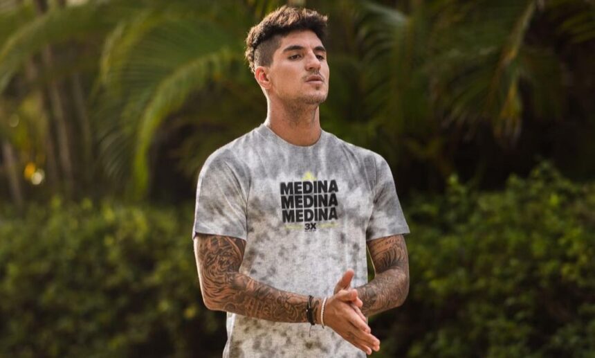 Gabriel Medina em uma foto na praia, utilizando uma camiseta branca estampada com sua marca