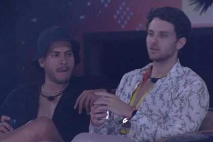 Lucas sentado ao lado de Arthur com uma latinha de bebida. Arthur de pernas cruzadas.