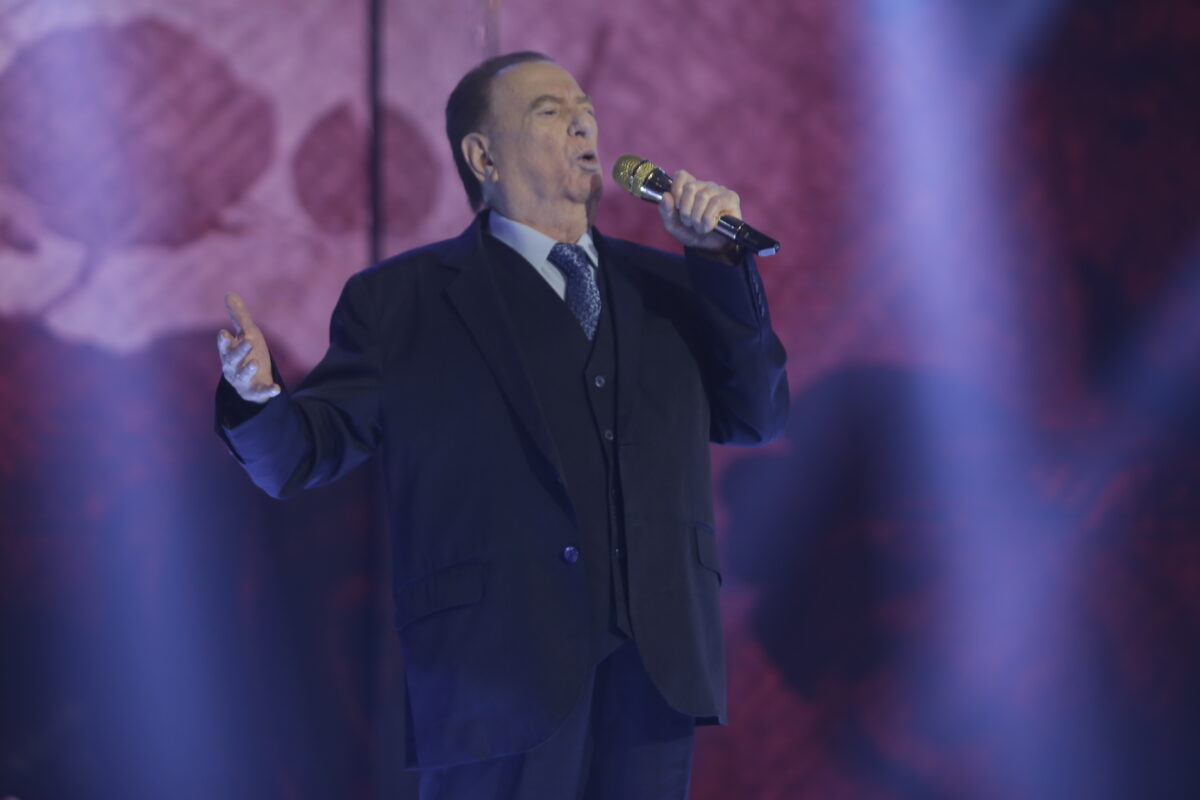 Raul Gil cantando nos estúdios do Programa Raul Gil, segurando um microfone na mão 