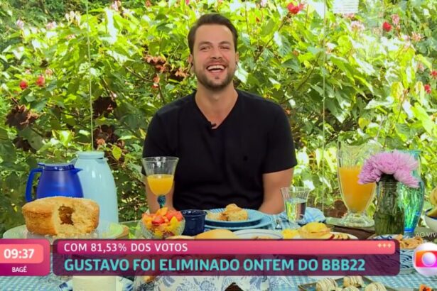 Gustavo sorrindo sentado de frente para uma mesa de café da manhã no Mais Você.