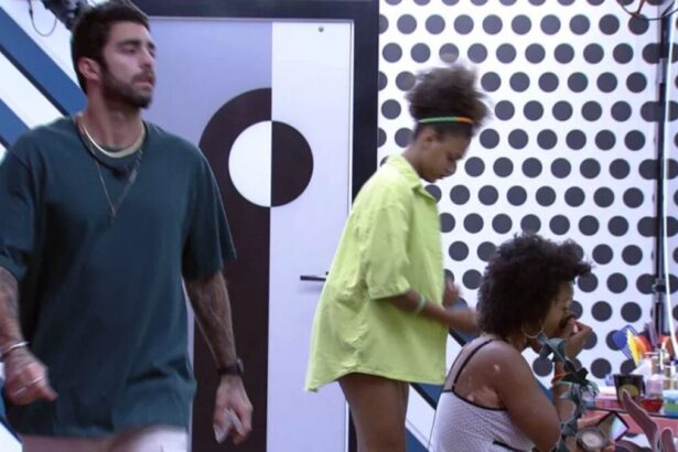 Scooby em pé de camiseta escura, Jessilane próxima a Natália que se olha no espelho.