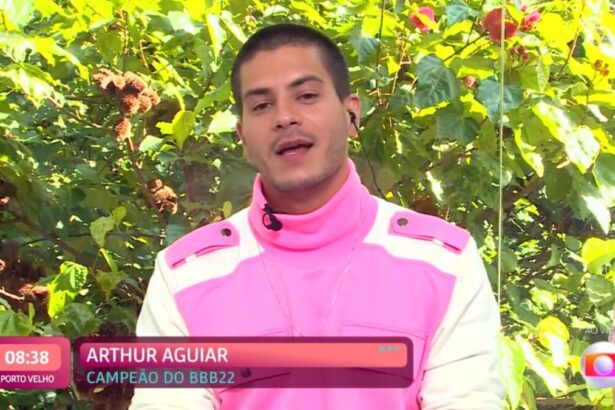 Arthur com uma roupa rosa com branco sentado numa mesa posta de café da manhã.