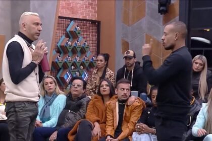Rogério de roupa preta com branca de frente para Mussunzinho vestido de roupa preta. Ao redor deles estão os participantes do Power Couple Brasil 6.
