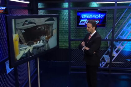 Jorge lordello em pé, de braços cruzados e em frente a uma televisão, nos estúdios do operação de risco, na redetv!