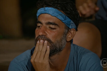 Matheus com a mão na boca e bandana azul na cabeça, reflexivo por estar no portal de eliminação