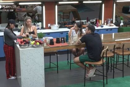 Eliza em pé no canto da mesa do Power couple ao lado de Karol. Em outra parte da mesa, Luana e Hadad sentados um de frente do outro.