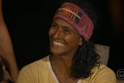 Flávia, de bandana roxa na testa, sorrindo, de camisa amarela, no portal de eliminação do No Limite