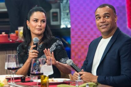 Luciele di Camargo de vestido preto, com o microfone na mão olhando para frente; Denilson de blazer azul e camisa básica branca com o microfone na mão olhando pra cima na gravação do Faustão da Band, da Band