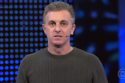 Luciano Huck vestindo um cardigã verde escuro, discursando nos estúdios do Domingão