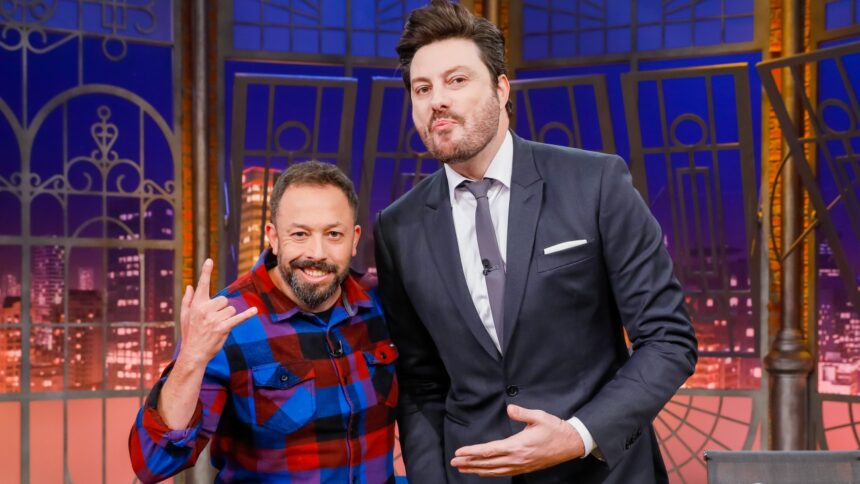 Fabio Gueré sorrindo, de camisa quadriculada azul e vermelha, fazendo símbolo do rock in roll com a mão direita ao lado de Danilo Gentili, que está de palitó e gravata, apontando para o humorista