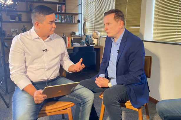 Allan Jesus frente a frente com Roberto Cabrini, em trecho da entrevista para a Record TV. Os dois estão sentados e o empresário segura o tablet nas mãos