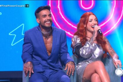 Matheus e brenda sentados nos estúdios da final do power couple brasil 6. Ela está com um microfone na mão