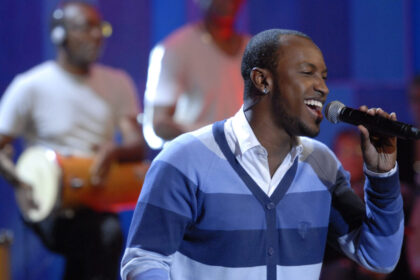Thiaguinho com um microfone nas mãos, se apresentando em um programa da TV Globo, com a banda ao fundo