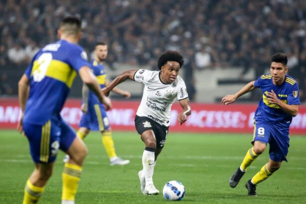Willian em campo com a camisa do Corinthians, tendo jogadores do Boca Juniors ao seu redor
