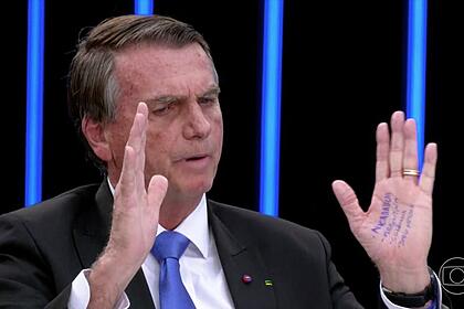 Bolsonaro em trecho da sabatina no jornal nacional, com os braços apertos em frente ao rosto