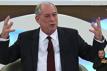 Ciro Gomes de palitó preto e gravata marrom, sentado, gesticulando durante entrevista no Roda Viva, da TV Cultura