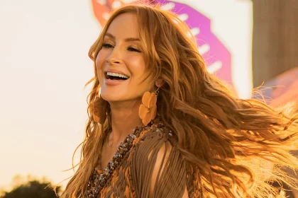 Claudia Leitte sorrindo, de top marrom e laranja, cabelo solto e brancos florais durante gravação de dvd