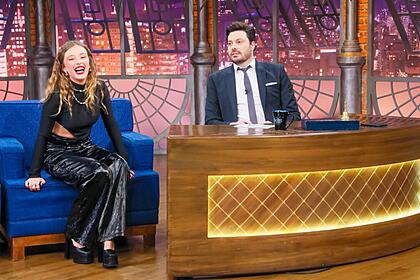 Duda Reis com top e calça preta, colar de prata, batom vermelho, cabelo solto durante gravação do The Noite, do SBT