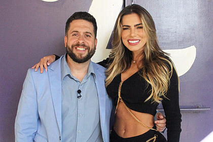 Erika Schineider de top e calça preta, cabelo solto, sorrindo, com a mão no ombro de Mauricio Meirelles; mauricio meirelles de blazer e camisa social azul, sorrindo, de barba, durante os bastidores da gravação do Foi Mau, da RedeTV! | Imagem: Reprodução/RedeTV!