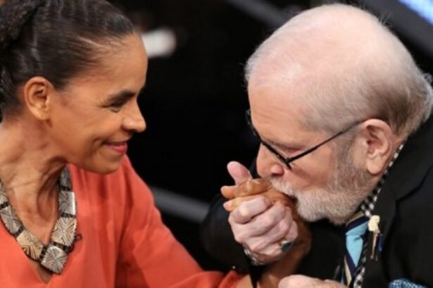 Marina Silva de colar, camisa vermelha, sorrindo, segurando a mão de Jô Soares durante gravação de programa de entrevistas na TV Globo