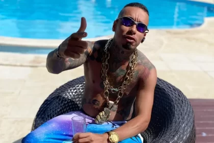 MC Kauan, sem camisa, com corrente de ouro, óculos esculo e apontando para a câmera