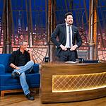 Marcos Pasquim de camisa social preta e calça jeans, sentado no sofá azul ao lado de Danilo Gentili durante gravação do The Noite, do SBT