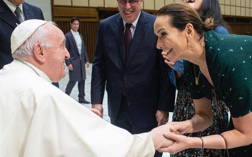 Maria Beltrão de vestido veste, abaixada segurando a mão do Papa Francisco durante encontro com o Papa Francisco no Vaticano