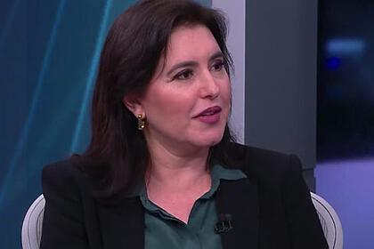 Simone Tebet de blazer preto, camisa verde, de cabelo solto e brinco discreto durante sabatina da CNN Brasil