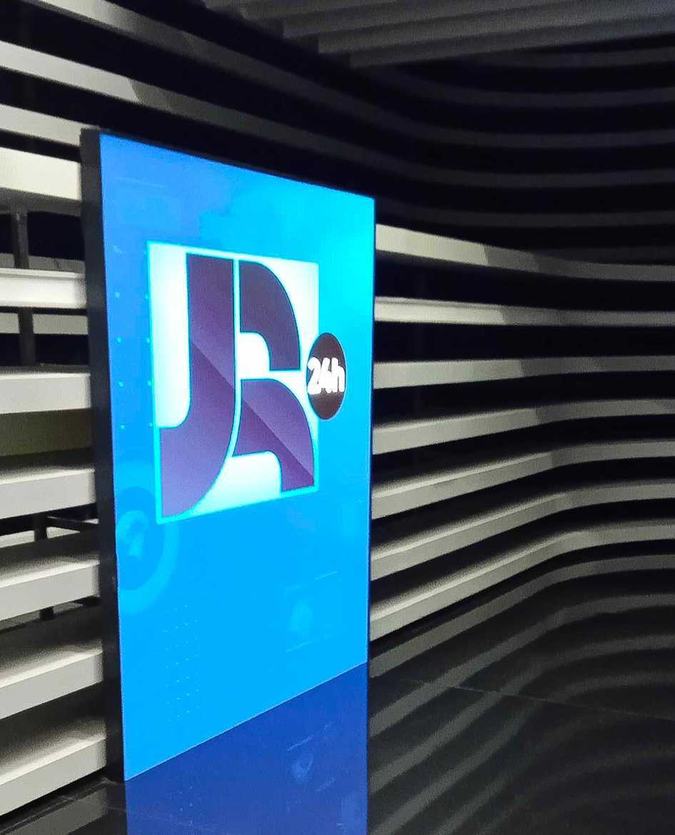 Telão menor e vertical dos estúdios do Jornal da Record, com o logo do telejornal acesso