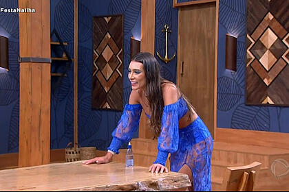 Whendy tavares em trecho do ilha record 2. Ela está com os braços sobre a mesa na vila