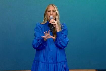 Adriane Galisteu com vestido azul segurando o microfone.