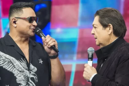 Xanddy Harmonia de camisa preta, óculos de sol, segurando o microfone em frente a Faustão durante gravação de programa