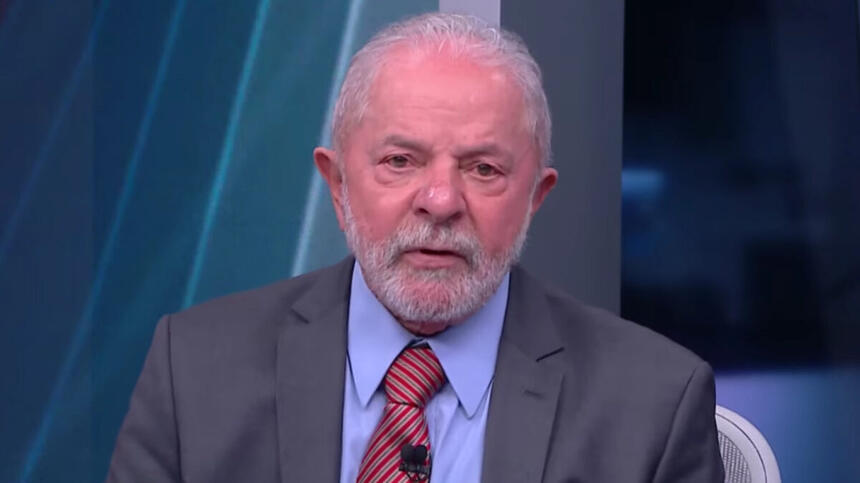 Lula de palitó cinza, gravata magenta e camisa social azul, com as mãos juntas, durante gravação da sabatina da CNN Brasil