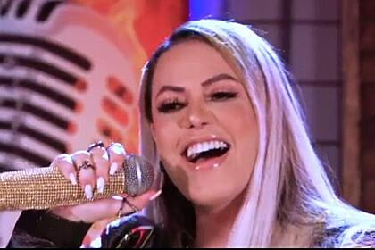 Michelle Melo de cabelo solto, boca aberta, com microfone dourado próximo; durante gravação do EP Risco de Embriaguez