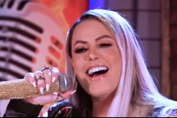 Michelle Melo de cabelo solto, boca aberta, com microfone dourado próximo; durante gravação do EP Risco de Embriaguez