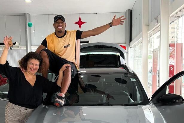 Paulo André sentado em cima de um carro, ao lado de sua mãe