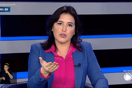 Simone Tebet de blazer azul, camisa social rosa, gesticulando durante entrevista na Record TV