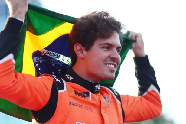 Felipe Drugovich segurando uma bandeira do Brasil acima da cabeça, ainda de macacão da Fórmula 2